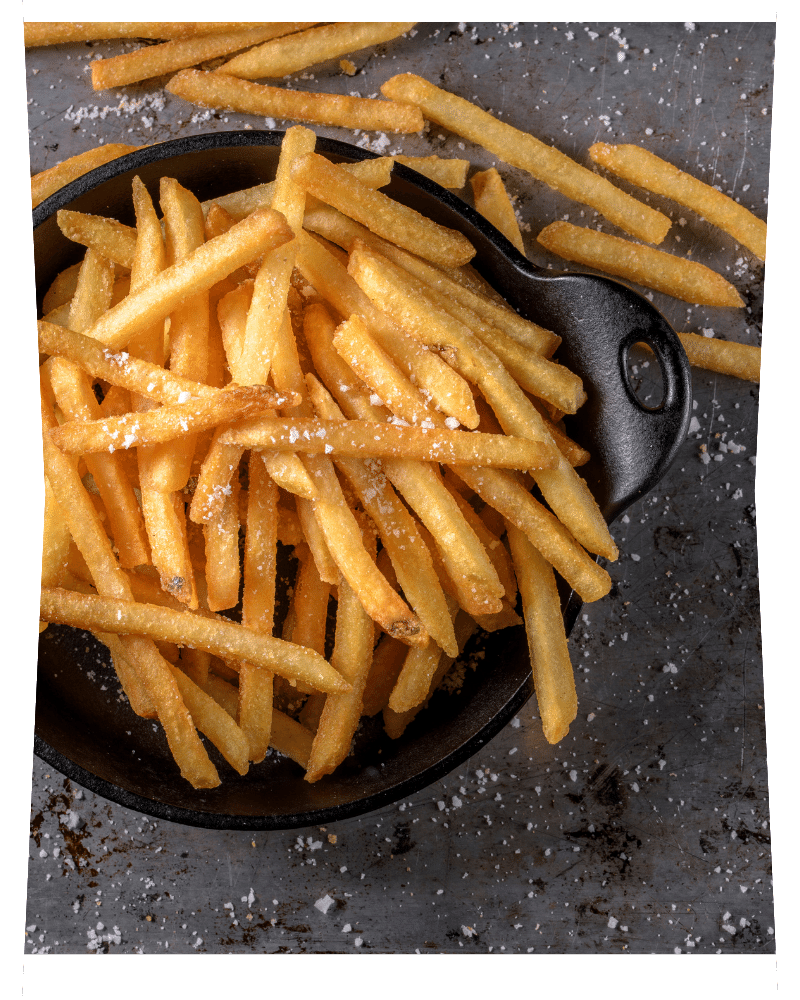 Portion de frites dans un plat en fonte noir et quelques frites renversées